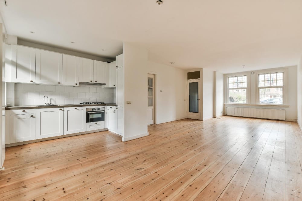 An empty apartment with white kitchen cabinets and wood floors.