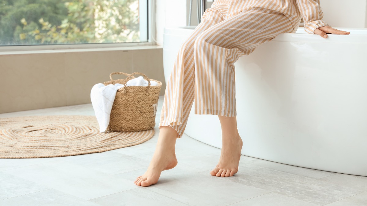 A person in striped pajamas sitting on the edge of a white bathtub