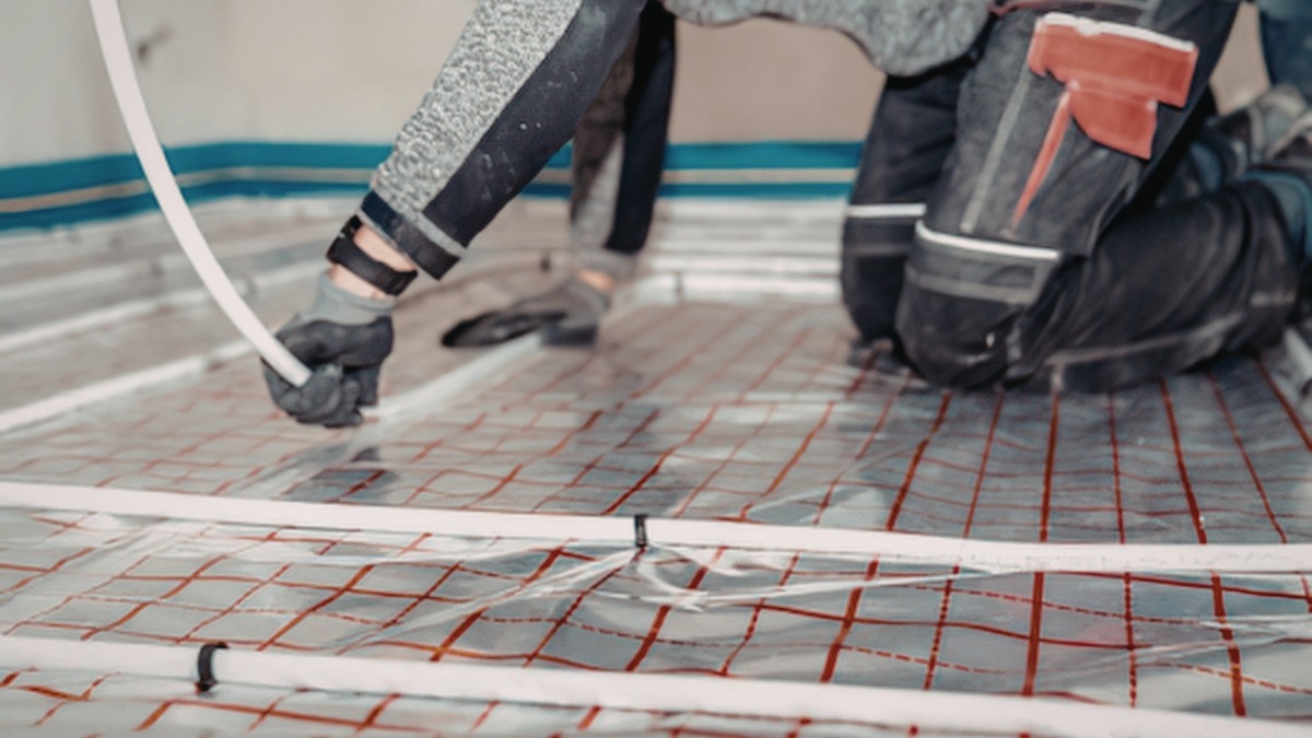 A worker installing white flexible tubing for underfloor heating